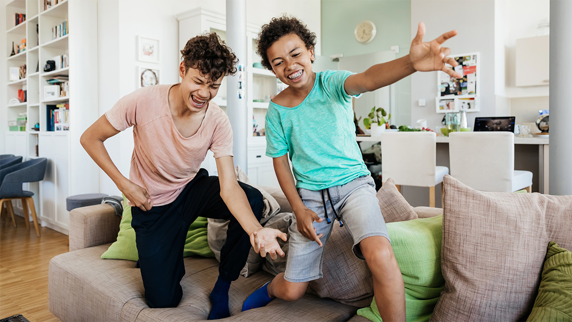 Two kids dancing and playing air guitar on a couch.