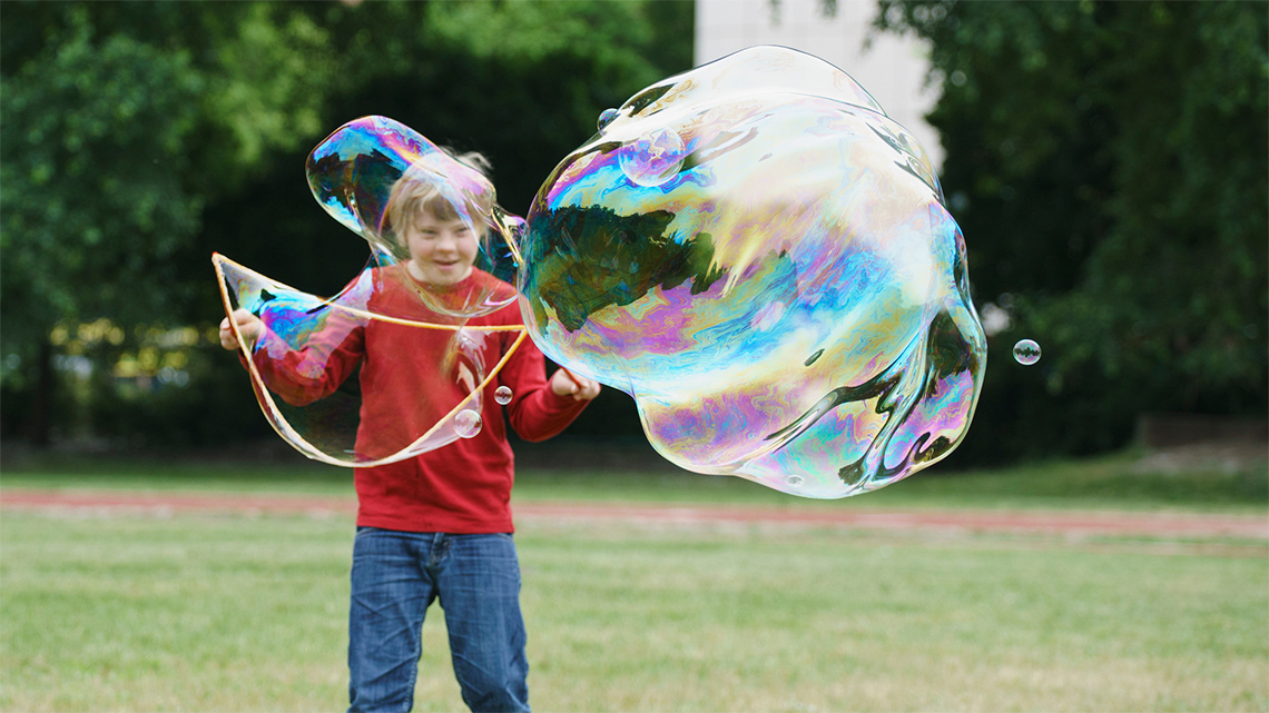 A kid playing outside with a bubble wand, making a large bubble.
