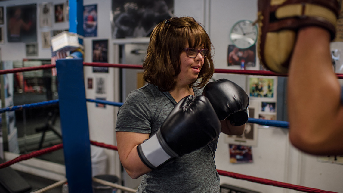 A teen standing in a boxing ring with gloves on.