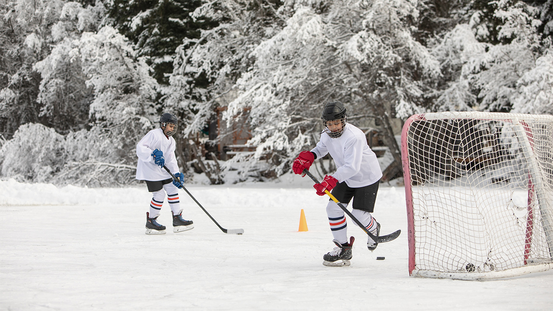 Two kids playing hockey on an outdoor skating rink in winter.