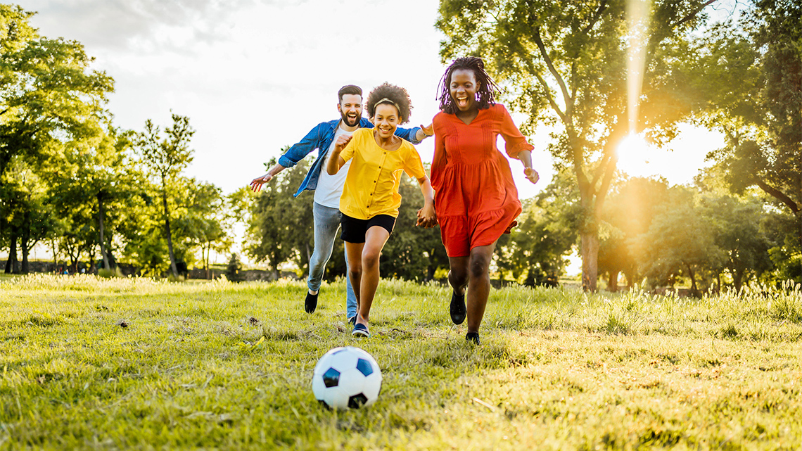 Two adults and a child playing with a soccer ball in a field.