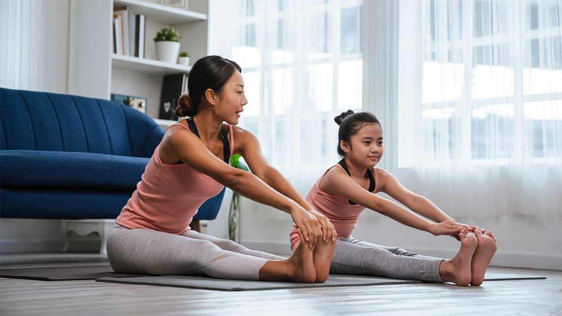 An adult and a child stretching on yoga mats in a living room.
