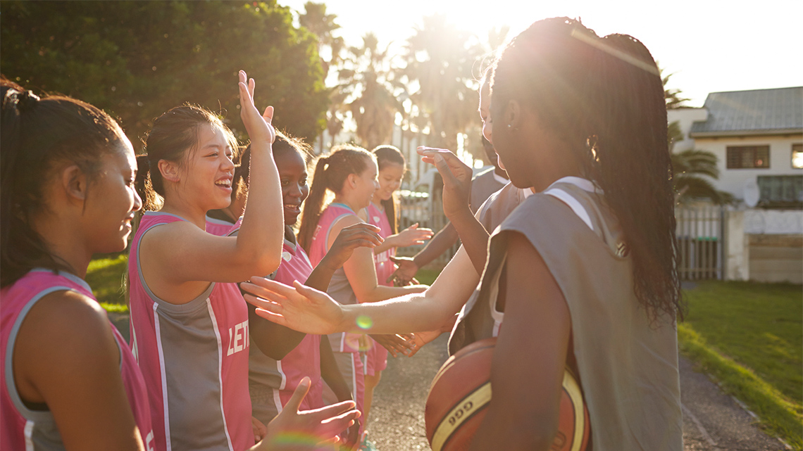 Several teammates from two basketball teams are lined up and taking turns high-fiving members of the opposite team.