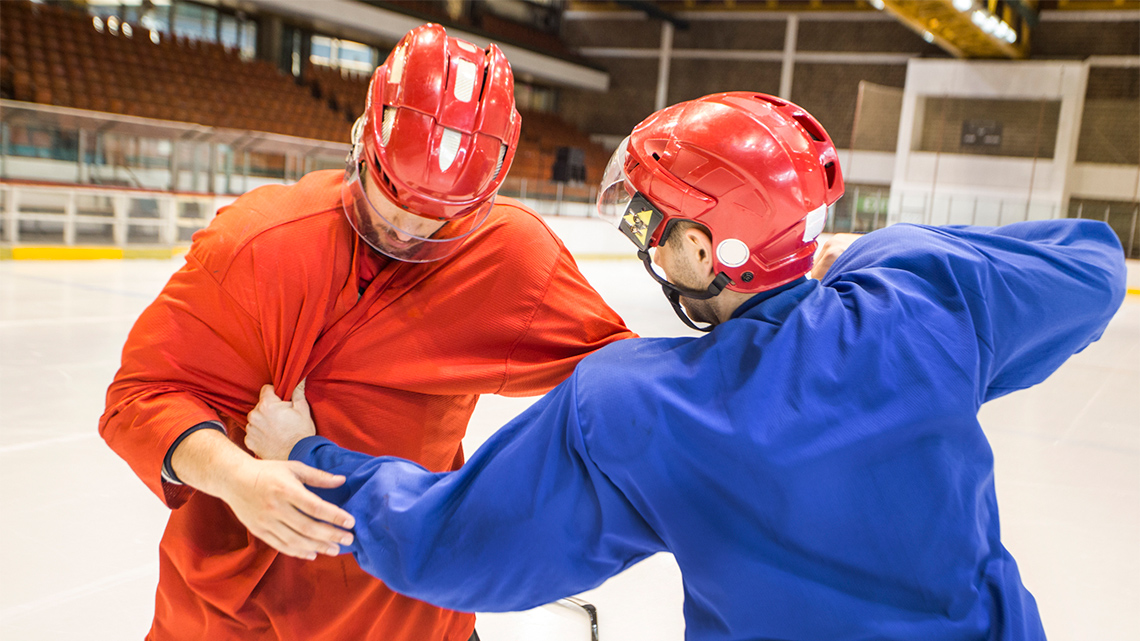 Two hockey players are grappling each other on a hockey rink. One player is grabbing the other by the jersey aggressively.