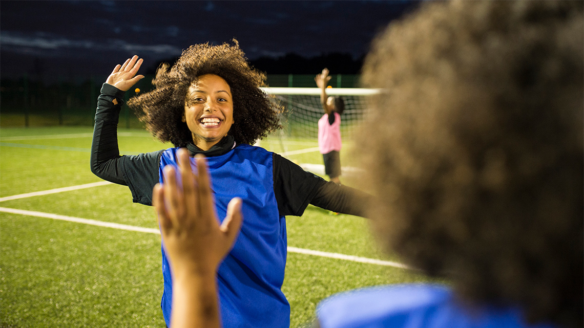 Two teammates on a soccer field, each with one hand raised to give a high-five.