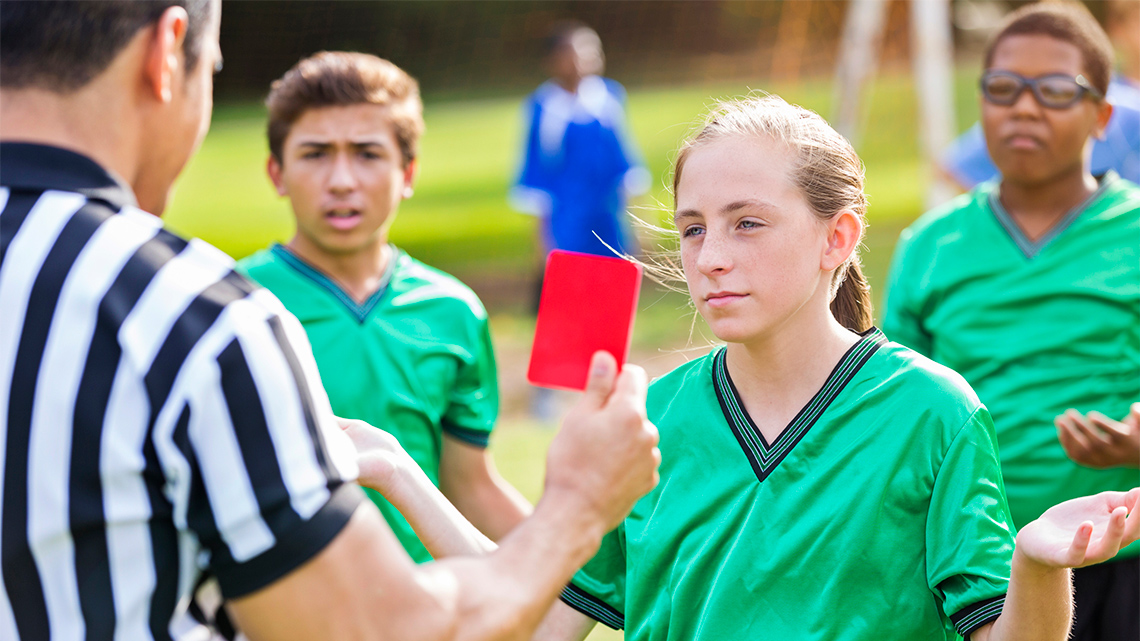 A referee shows an athlete a red penalty card; the athlete and two teammates are frowning and shrugging.