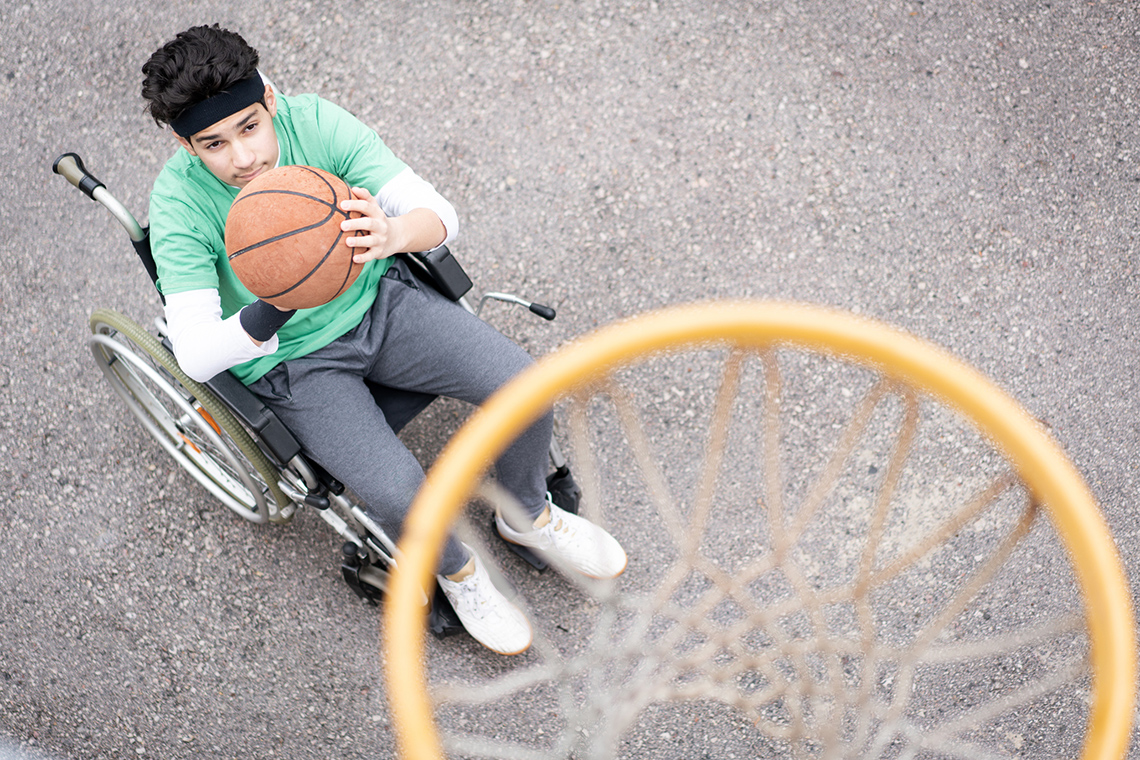 Student sitting in a wheelchair while shooting a basketball in a net on a basketball court.