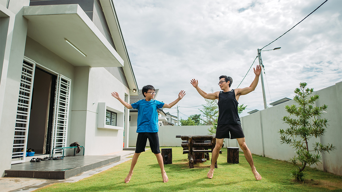 Two people doing jumping jacks in a backyard, jumping while raising their arms over their heads..