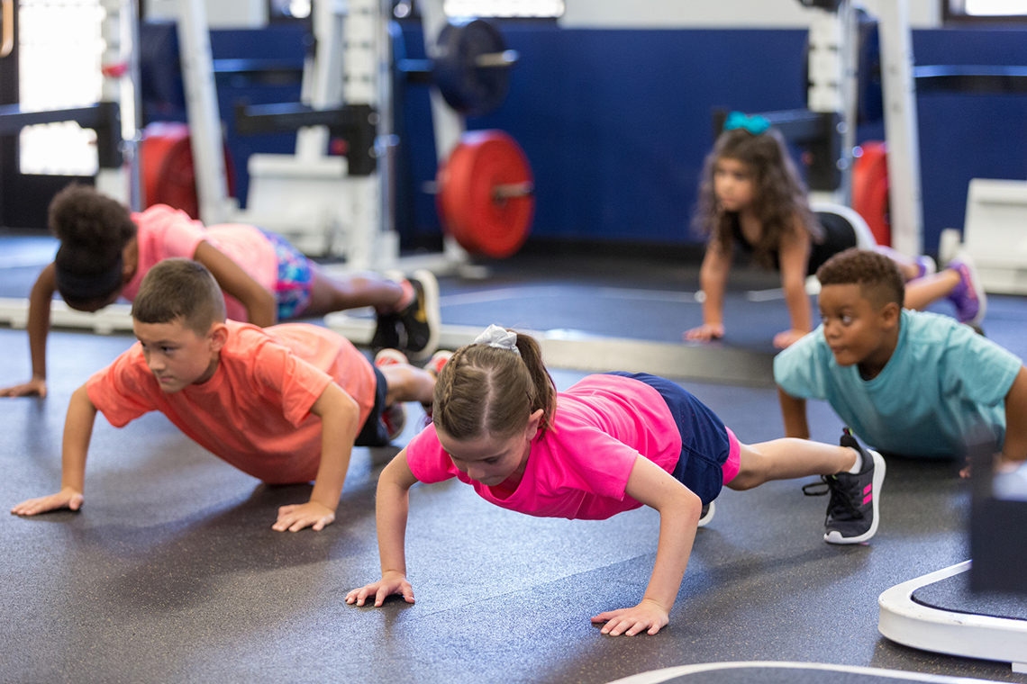 Student in gym class performing a body weight exercise, push ups with peers.