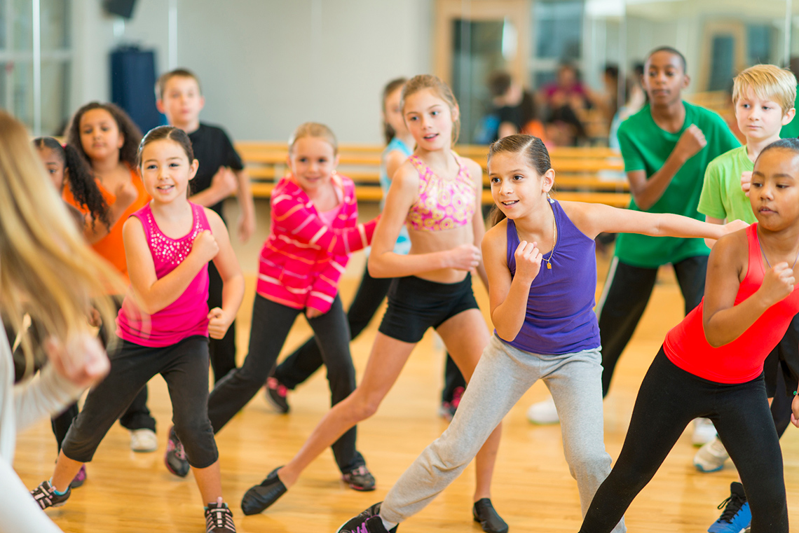 Children dancing in gym and following teacher’s movements.