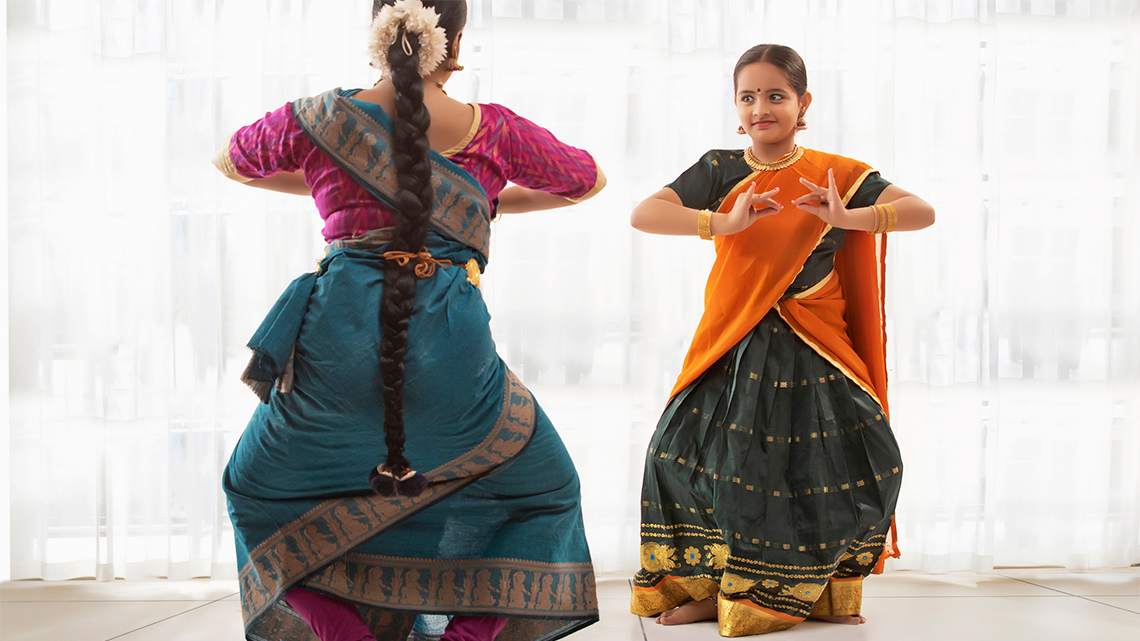 Bharatanatyam student with teacher in traditional and colourful clothing.