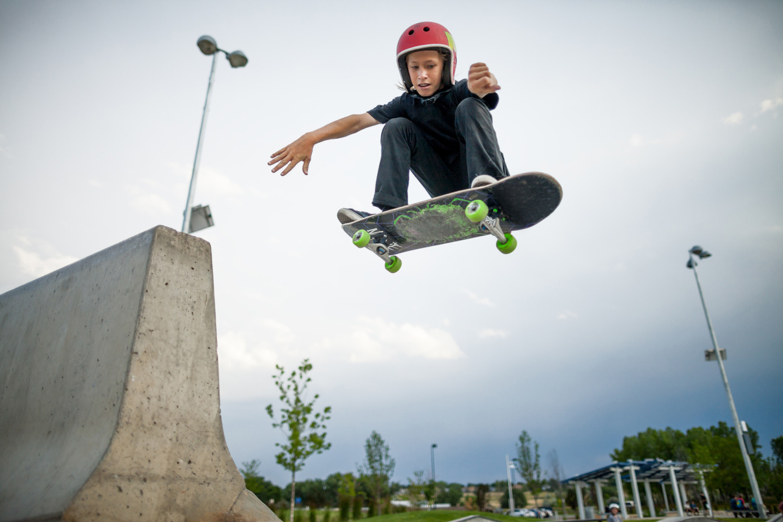 A skateboarder wearing a helmet performs an aerial trick on their skateboard at an outdoor skateboard park.