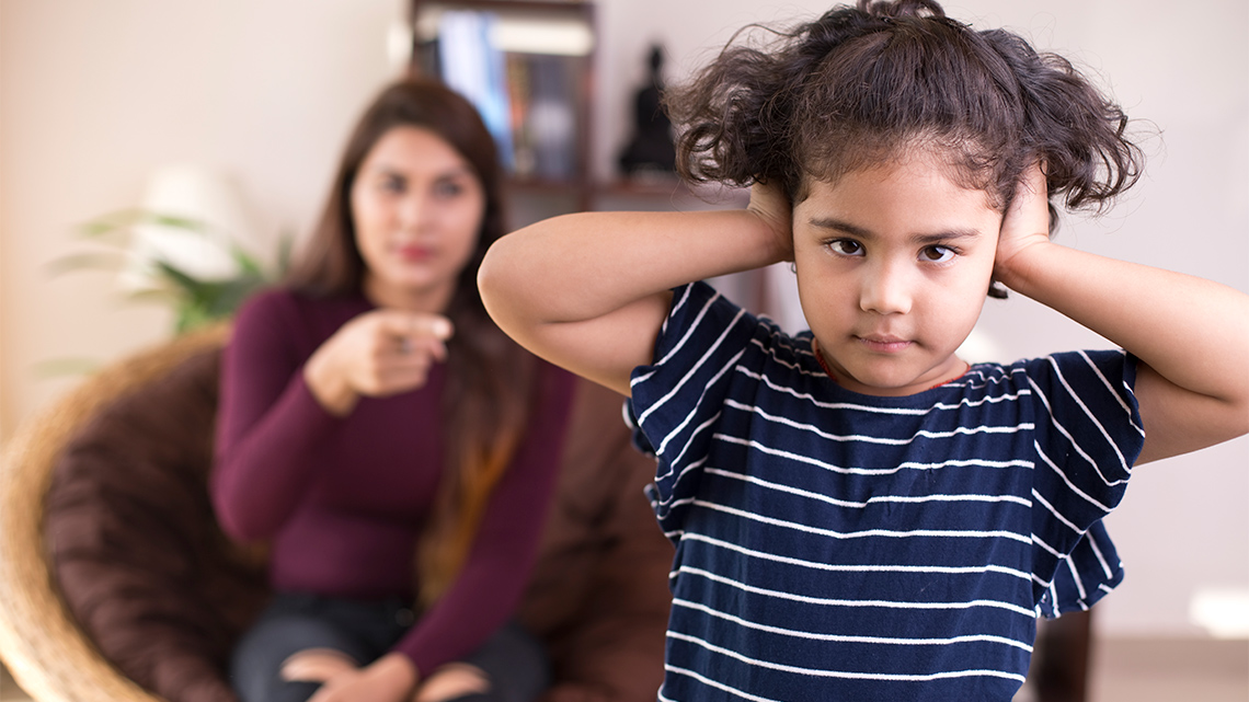 A child covering their ears and turning their back to an adult that is speaking to them.