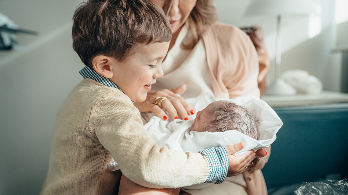 A child gently holding a baby that is being passed to them by an adult.