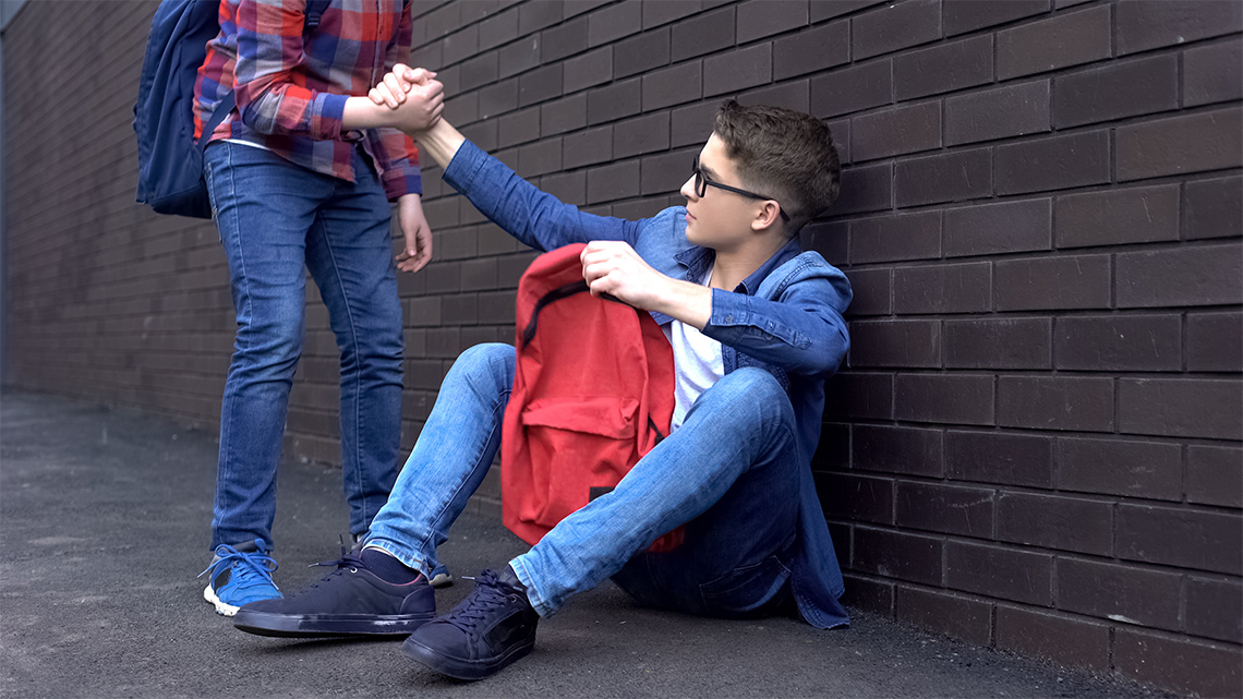 One child grabbing another child’s hand to help them get up off the ground.