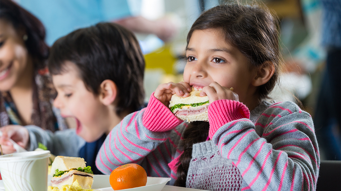 A child is sitting at a lunch table and taking a bite out of a sandwich