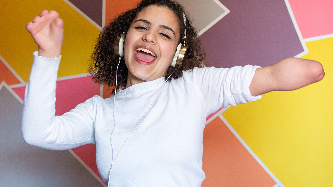 A child with an amputated hand and fingers is singing and dancing while wearing headphones