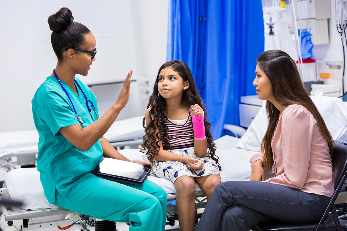 A doctor speaks to a child with an arm cast and their guardian in a hospital