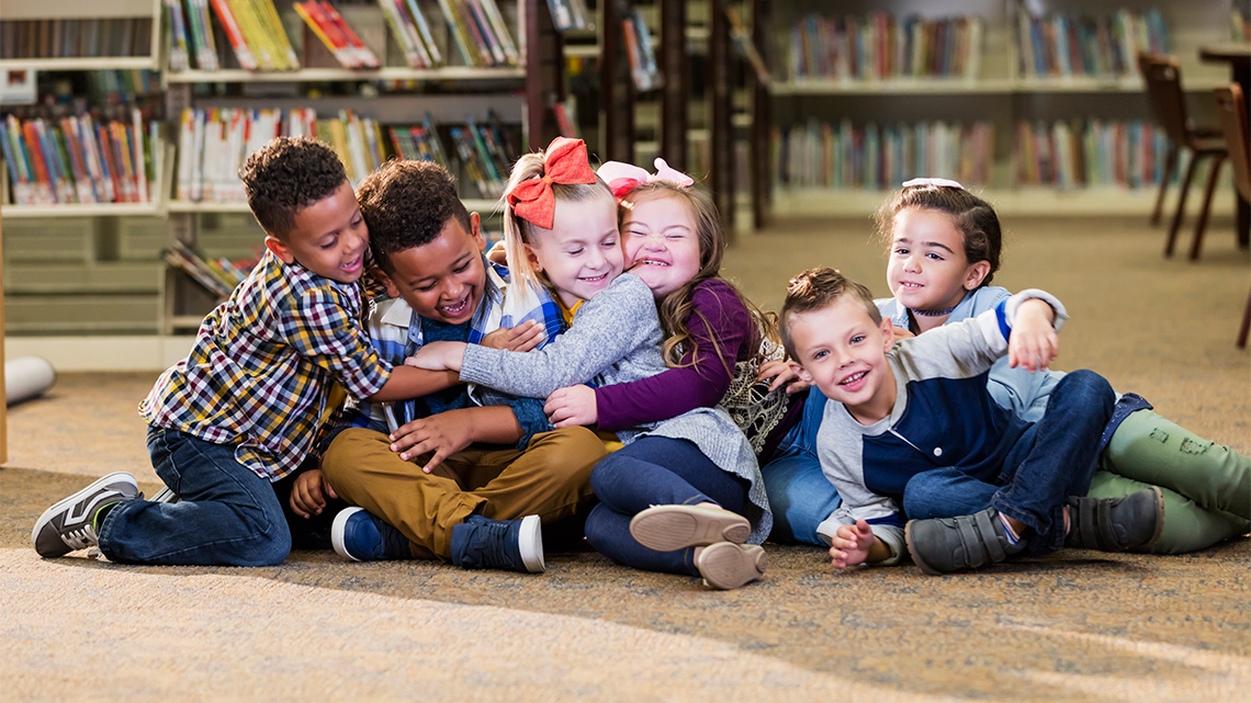 A group of children are playing and hugging on the floor in a library.
