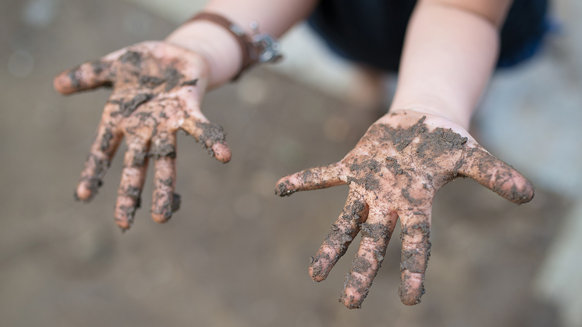 A child holding out their hands covered in mud.