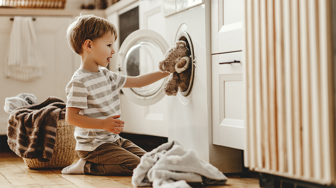 A child putting a stuffed bear into a washing machine.