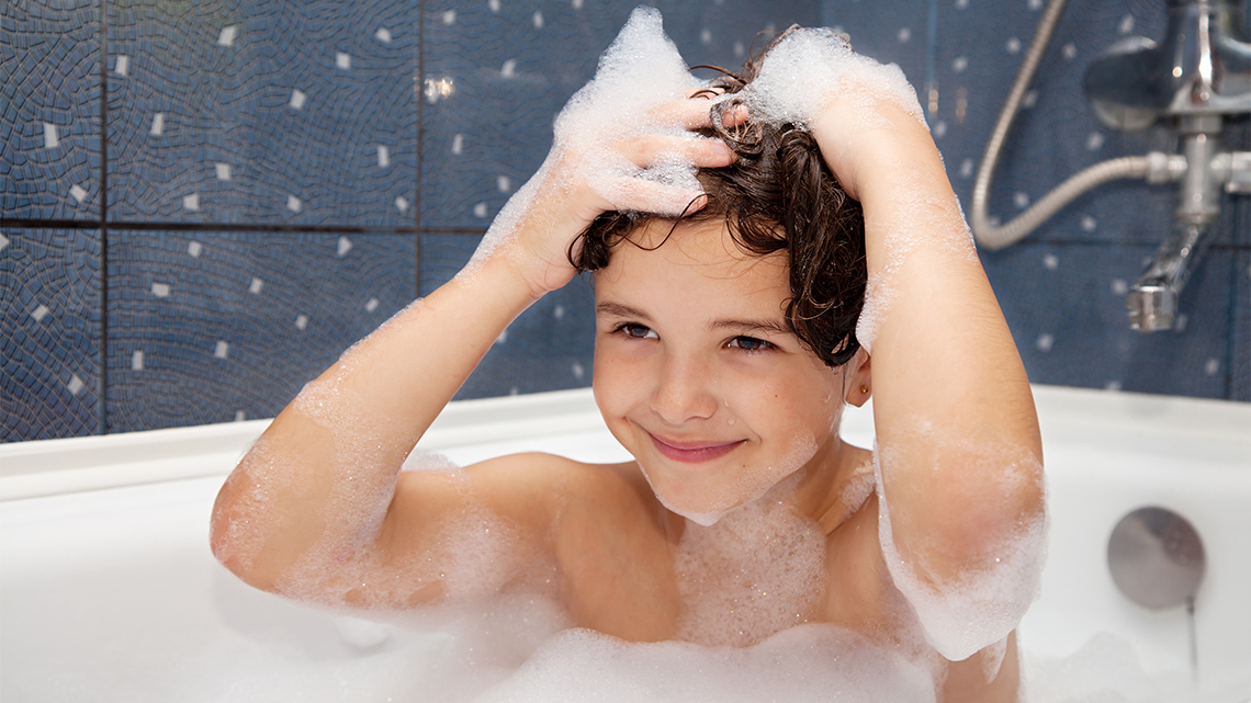 A child washing their head with shampoo in a bathtub.