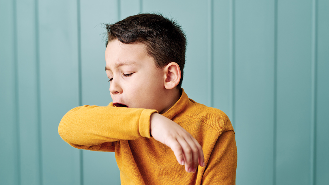 In this image a child is coughing into the sleeve of their shirt.