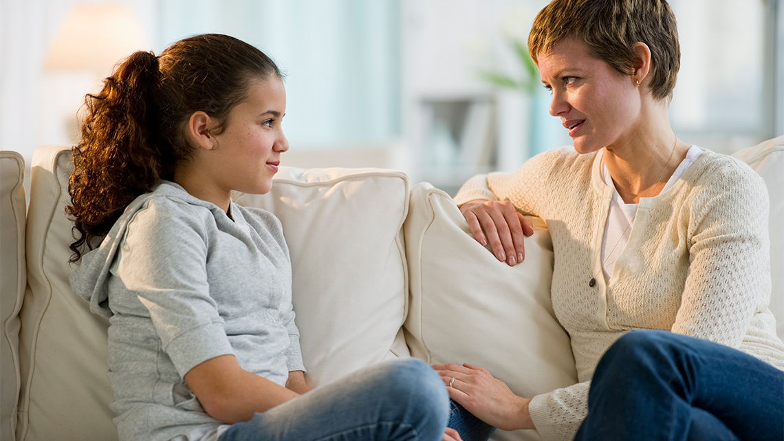 An adult and child sitting on a couch having a serious conversation.