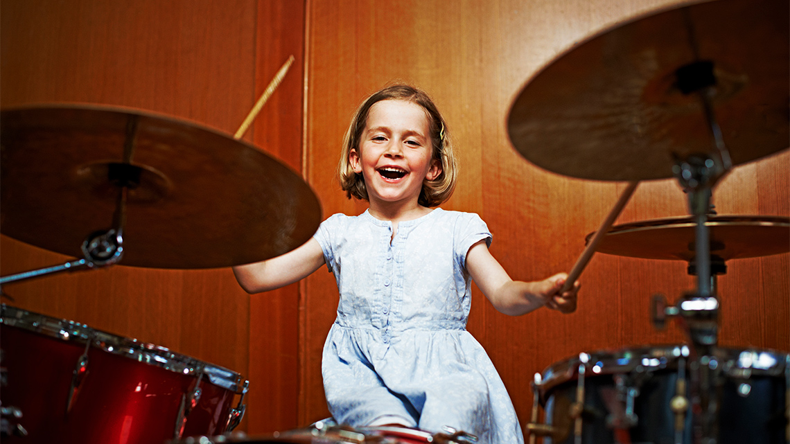 A child playing the drums and smiling.