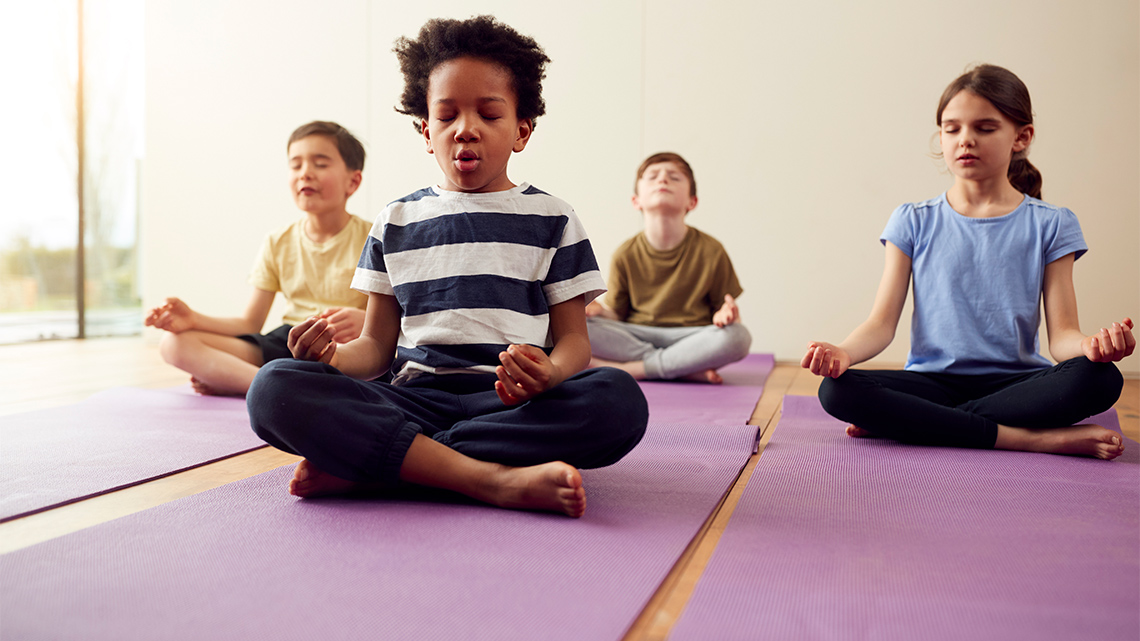 Children sitting on mats with their legs crossed and eyes closed, taking deep breaths.