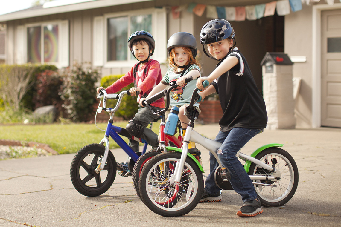 Three children on bicycles with their helmets on.