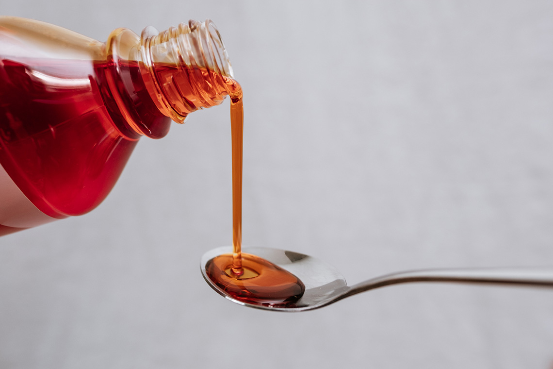 Cough syrup is being poured from a bottle onto a spoon.