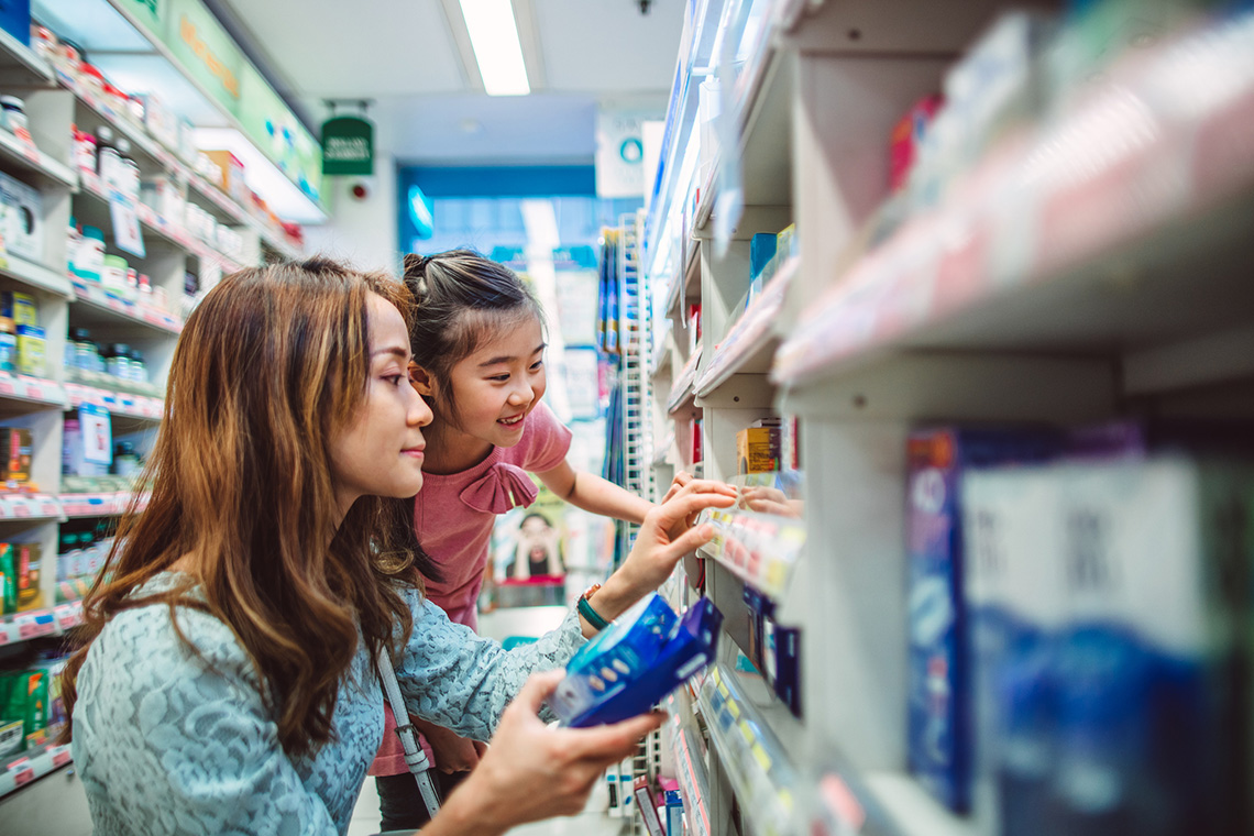 An adult and a child are looking at over the counter medications in a drugstore.