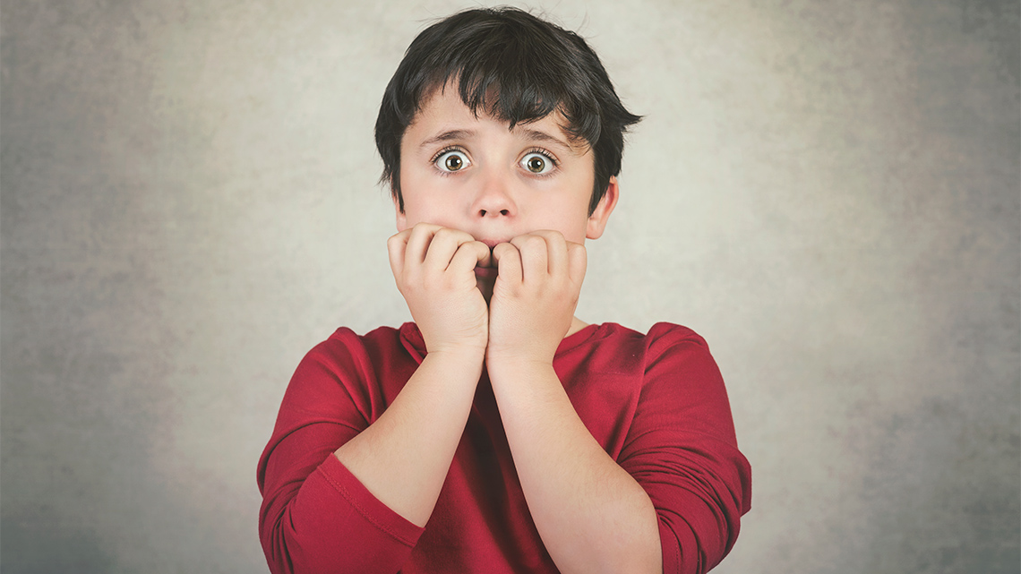 A child is holding their hands in front of their mouth and their eyes are open wide.
