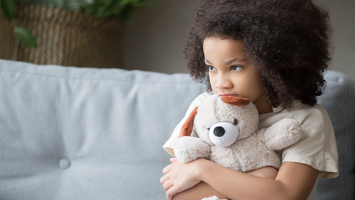 A child looking sad, holding a stuffed bear.