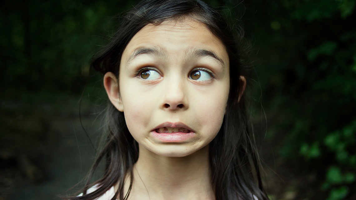 A child grimacing with raised eyebrows, looking off into the distance.