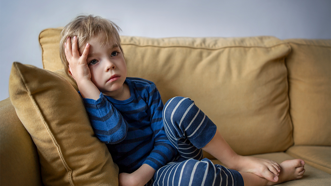 A child looking sad on a couch, resting their head in their hand.