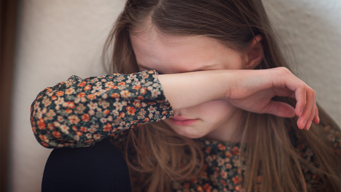 A sad child holding her arm across her face.
