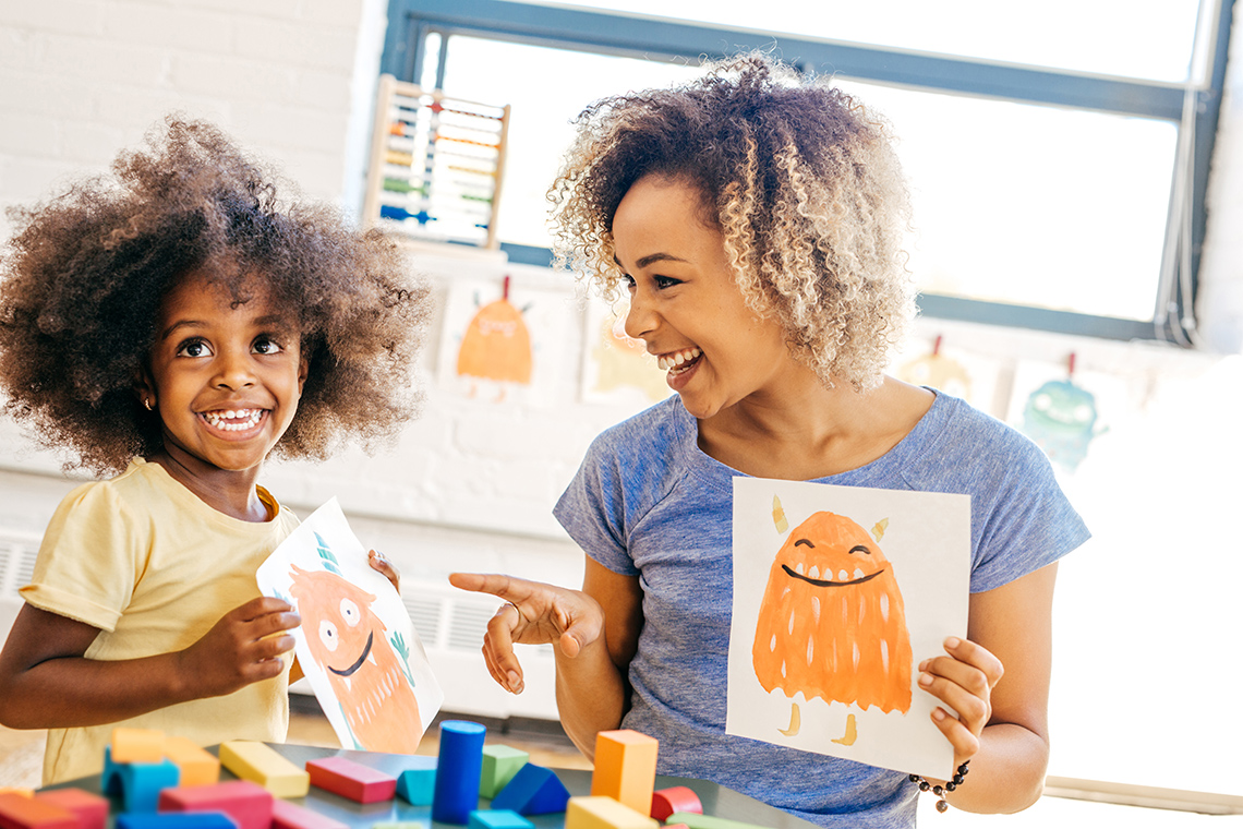 A child and an adult are holding up their artwork and smiling.