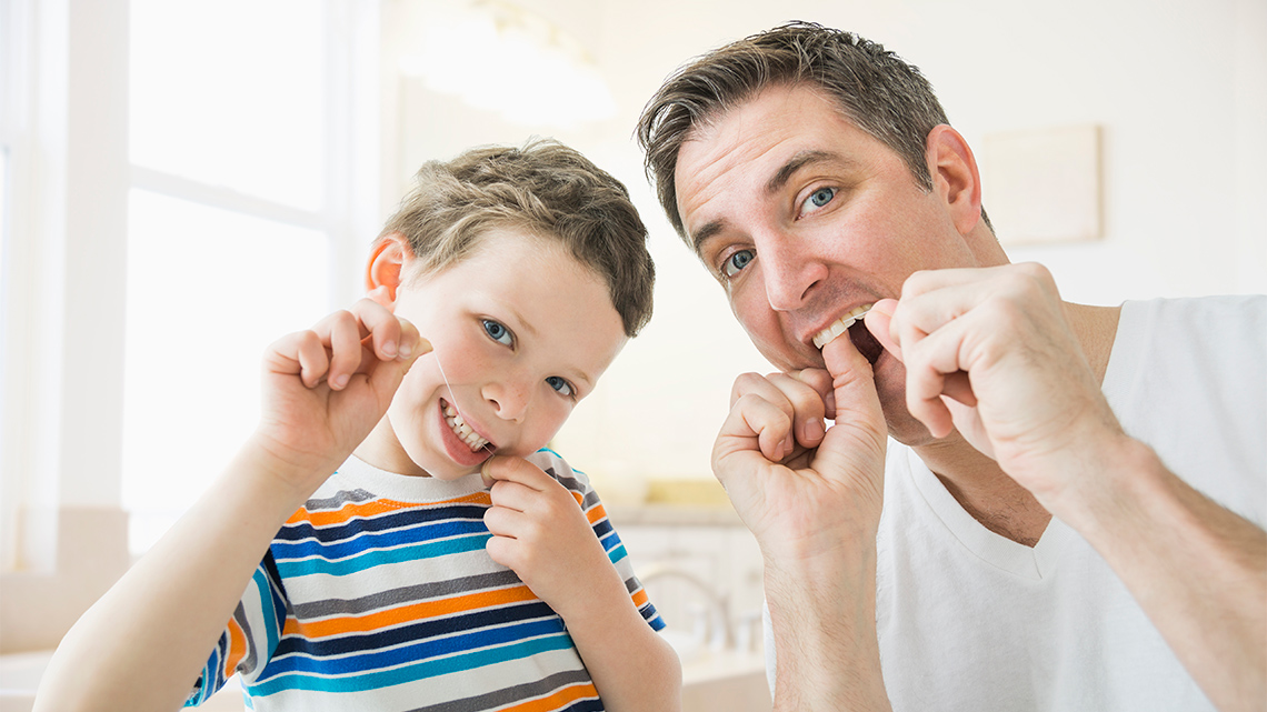An adult and child flossing their teeth together.