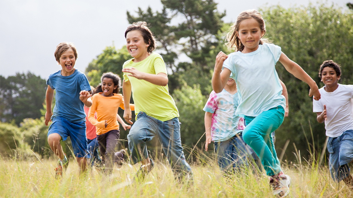 Group of children playing and running together through a field.