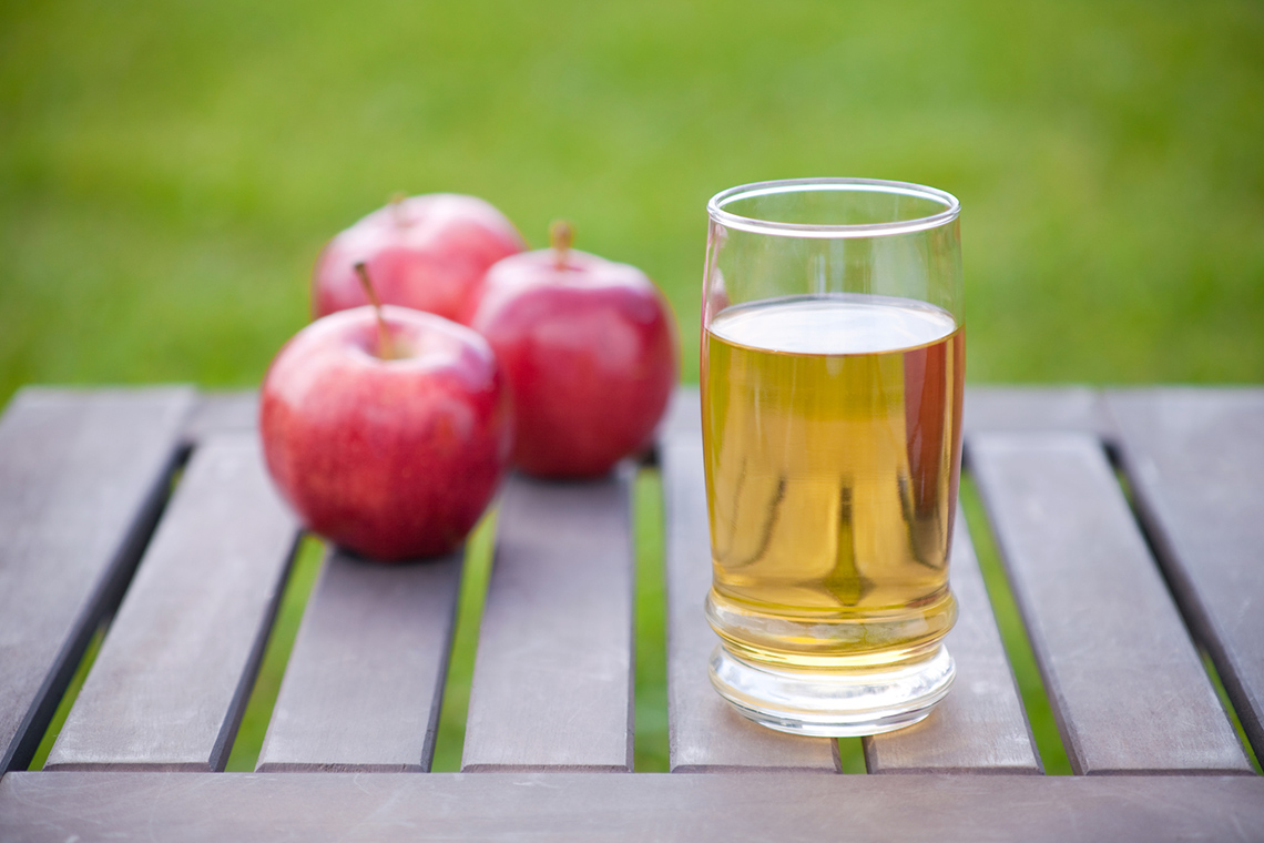 3 apples and a glass of fresh apple juice on a table.