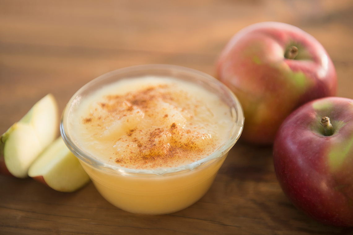 Bowl of apple sauce with cinnamon, surrounded by apples and sliced apples.