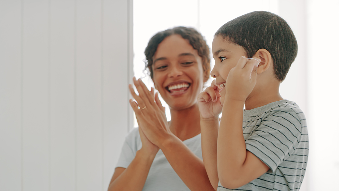 A child flossing their teeth while an adult looks on.