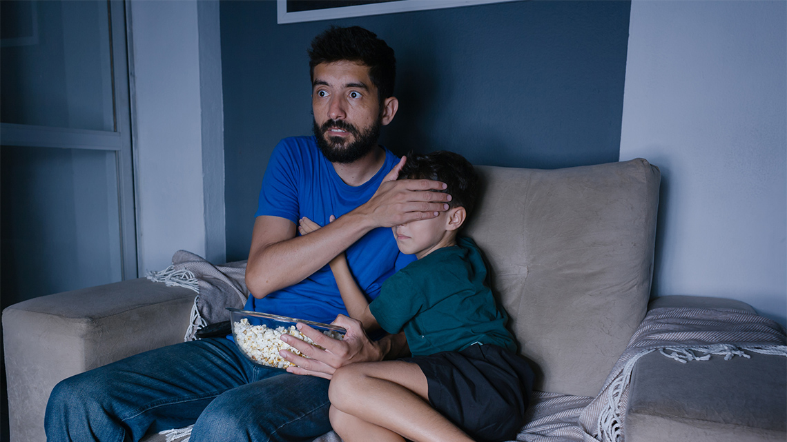 An adult covering the eyes of a child while watching a scary movie.