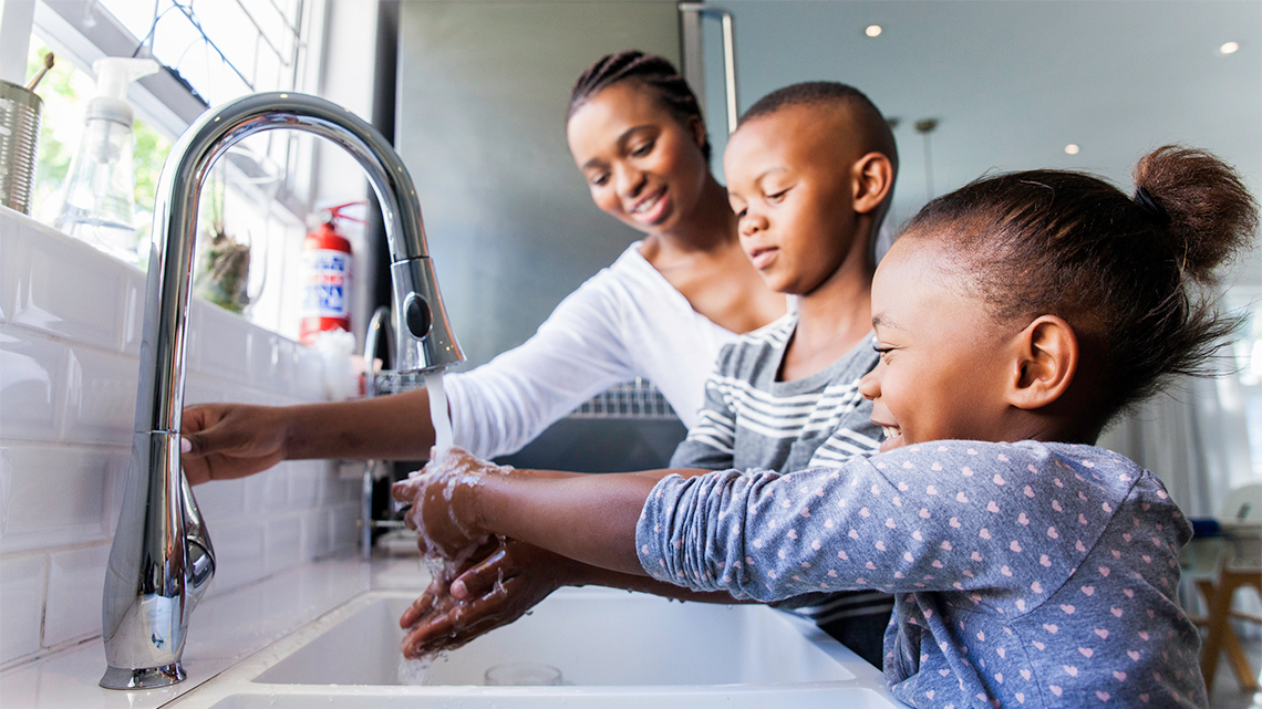 Two children and an adult washing their hands.