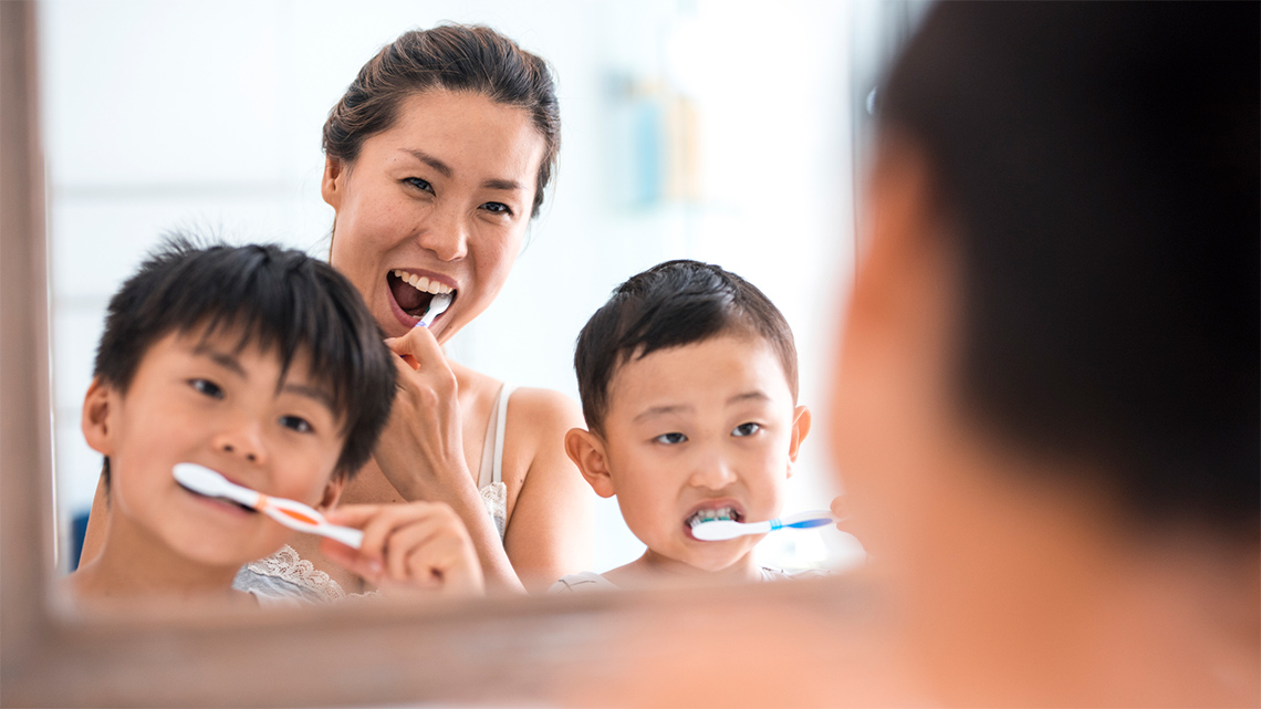 Two children and an adult brushing their teeth together.