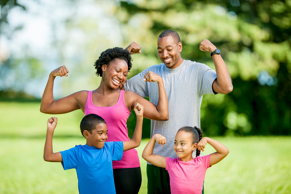 There are two adults and two children. All four are smiling and flexing their muscles.