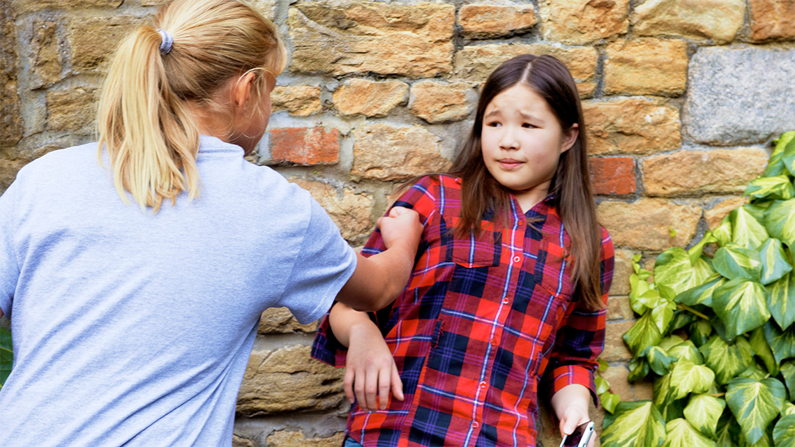 A youth who looks scared stands against a wall while another youth is holding a fist towards them.