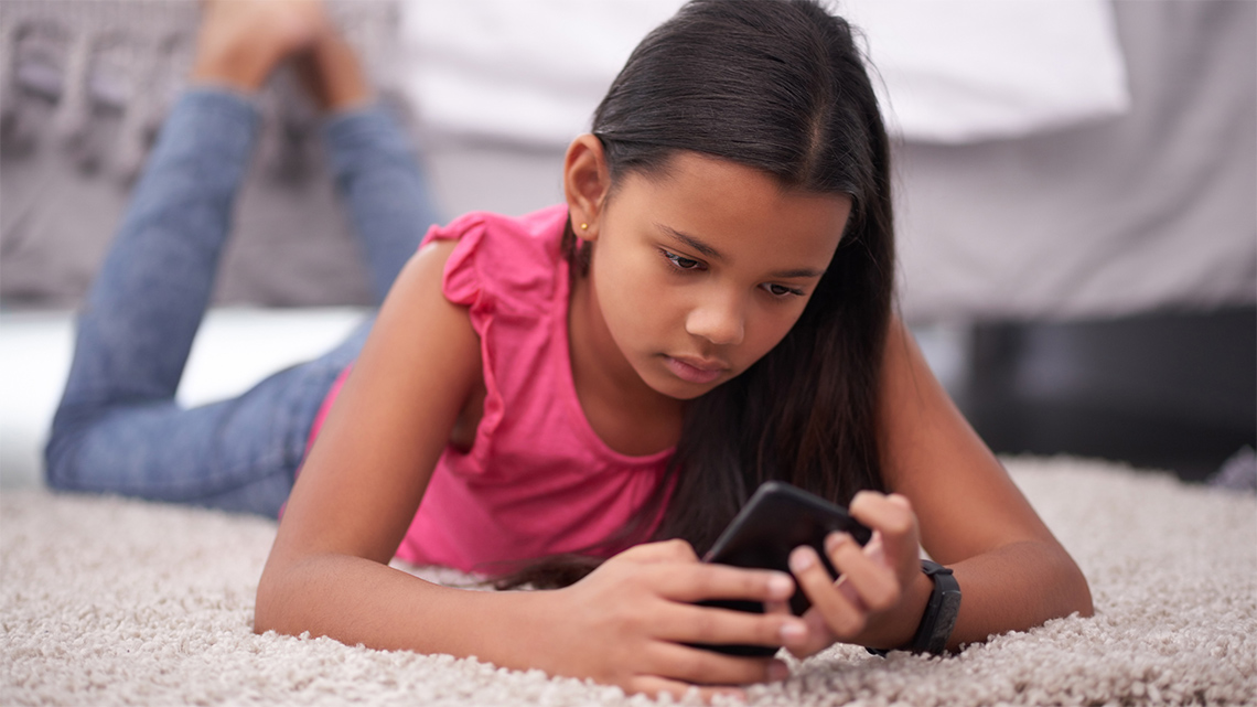 A youth lying on the floor with their phone in their hands. They have a worried look on their face.